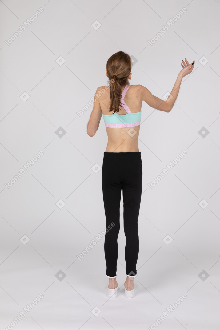 Back view of a teen girl in sportswear balancing on her leg raising her hand while questioning