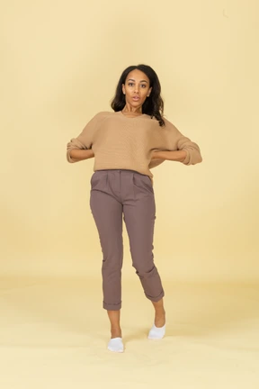 Front view of a dark-skinned young female putting hands on hips & leaning back