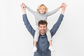Boy sitting on his father's neck with their hands up