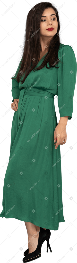Three-quarter view of a young lady in green dress putting hand on hip