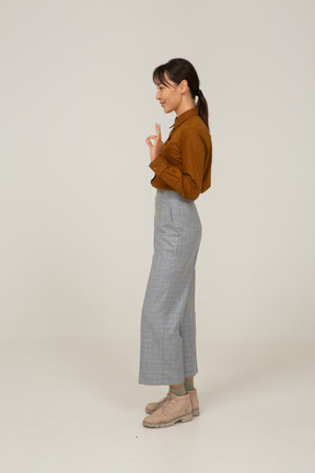 Vista lateral de uma jovem mulher asiática de calça e blusa, mostrando um gesto de ok