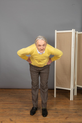 Front view of an old man putting hands on hips while leaning forward