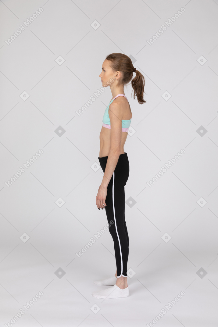Vista lateral de una jovencita en ropa deportiva de pie y mirando hacia arriba