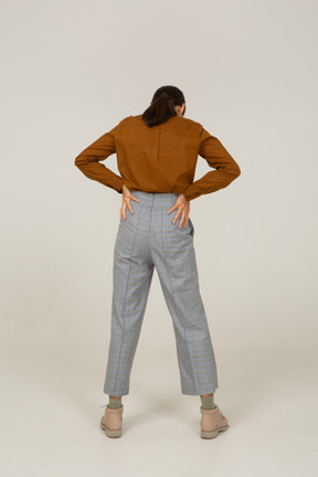 Vista posteriore di una giovane donna asiatica in calzoni e camicetta che mette le mani sui fianchi