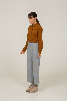 Vista di tre quarti di una giovane donna asiatica in calzoni e camicetta che stringe i pugni