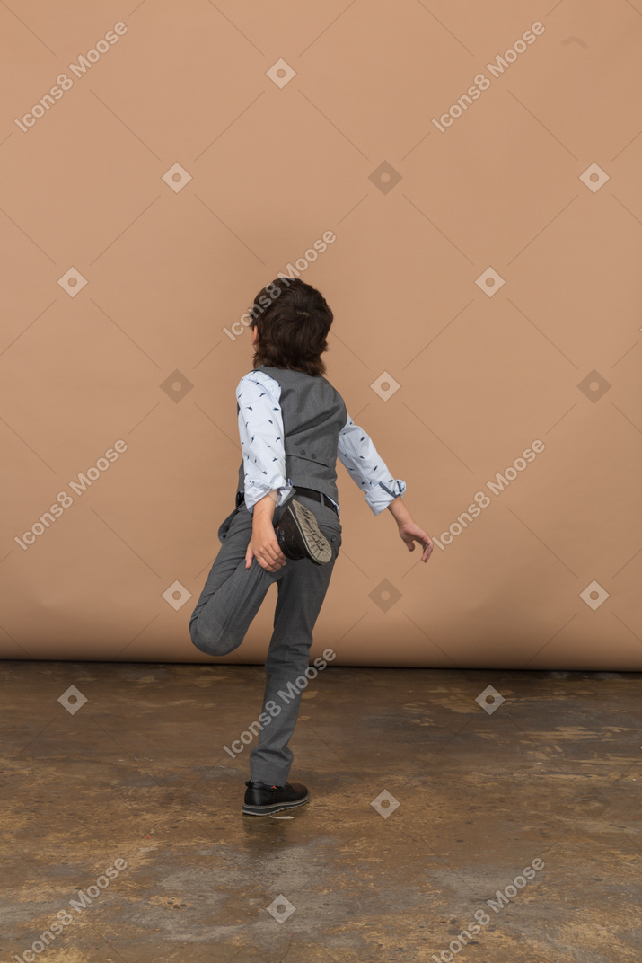 一个穿着西装的男孩单腿站立的后视图