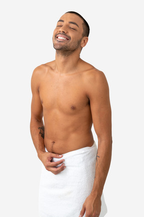 Contented barechested young man standing wraped in towel