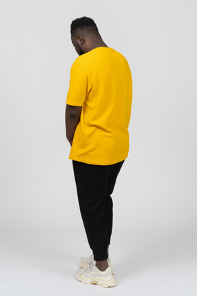Three-quarter back view of a withdrawn young dark-skinned man in yellow t-shirt