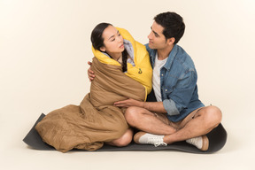 Young woman wrapped in sleeping bag and man sitting on karimat