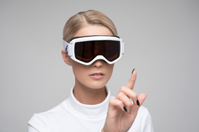 Jeune femme dans des lunettes de ski touchant quelque chose de virtuel