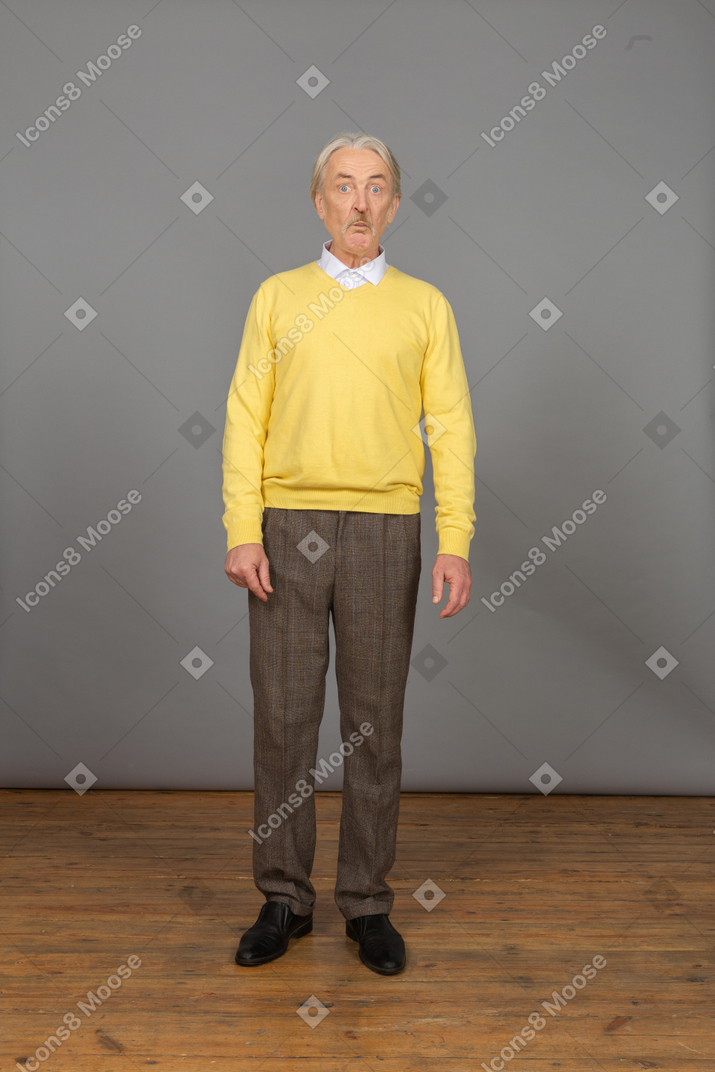 Vista frontal de um velho surpreso de blusa amarela, olhando para a câmera e fazendo uma careta