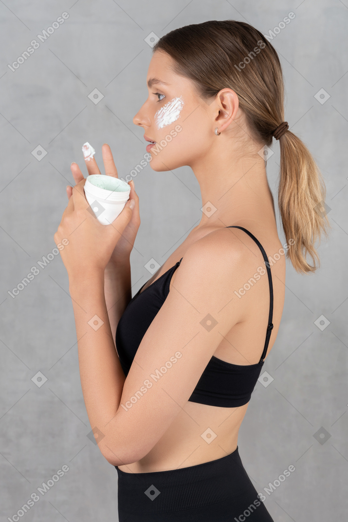 Vista laterale di una giovane donna con la crema sul viso