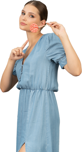 Трехчетвертный вид молодой женщины в синем платье, держащей леденец