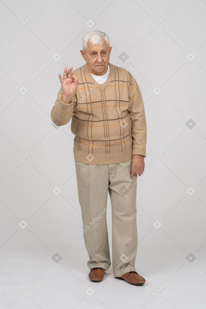 Vista frontal de un anciano con ropa informal que muestra el signo de ok