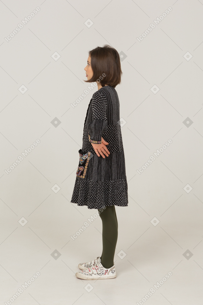 Side view of a funny little girl in dress showing tongue and putting hands on hips