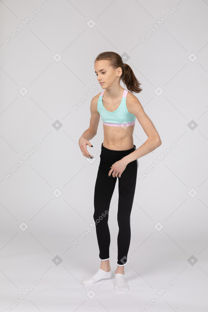 Вид в три четверти слабой девушки-подростка в спортивной одежде, наклонившейся вперед и жестикулирующей