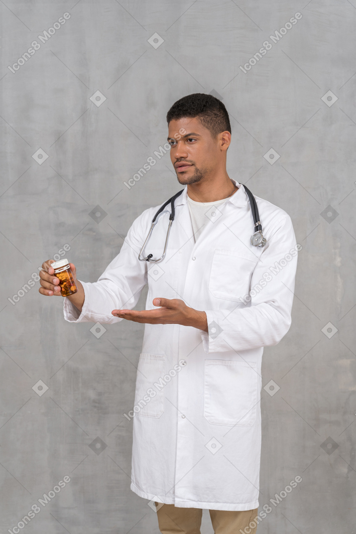 Jovem médico apontando para um frasco de comprimidos