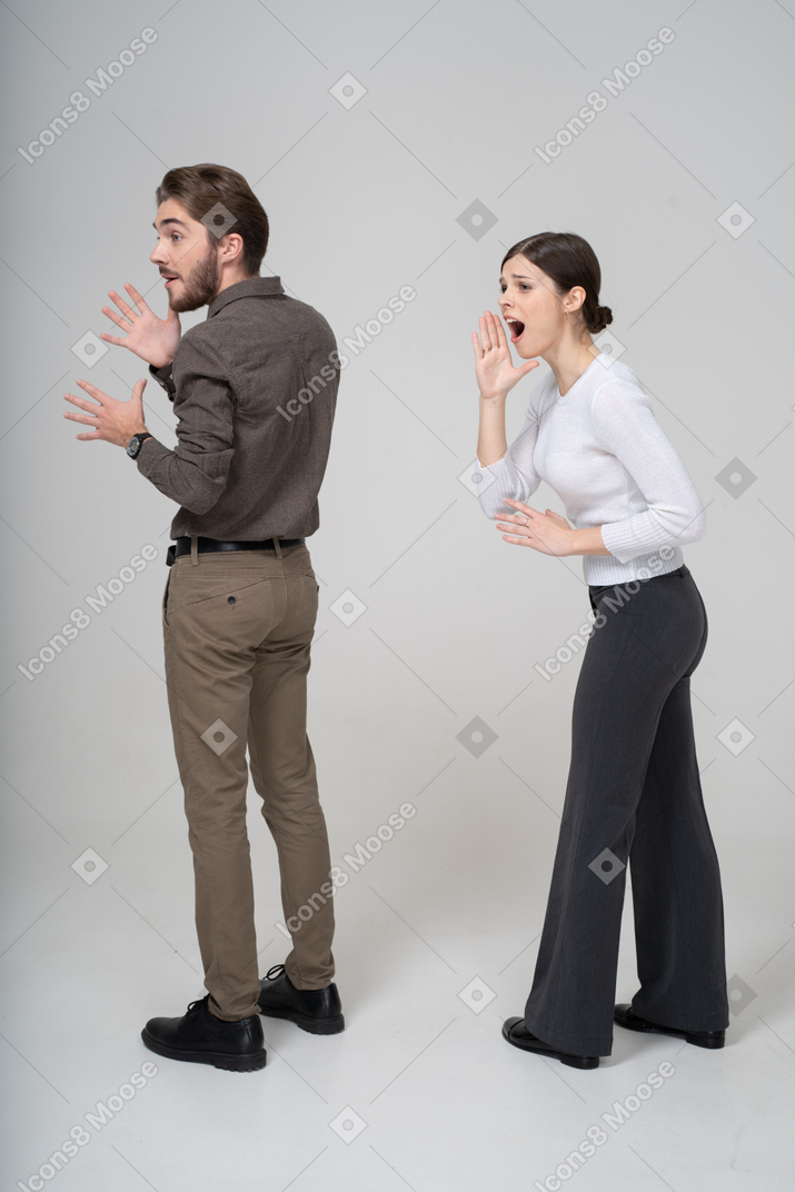 Vista posterior de tres cuartos de una joven pareja gesticulante emocional en ropa de oficina