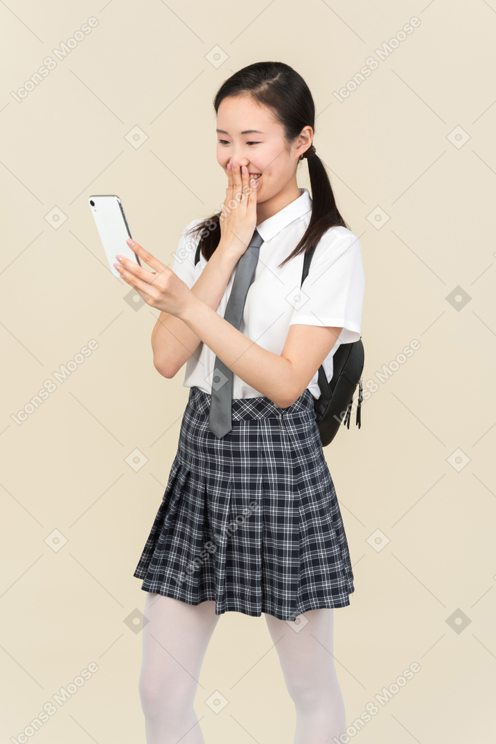 Laughing asian school girl looking at smartphone