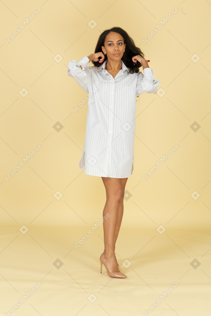 Vista frontal de uma jovem mulher de pele escura em um vestido branco arrumando o cabelo