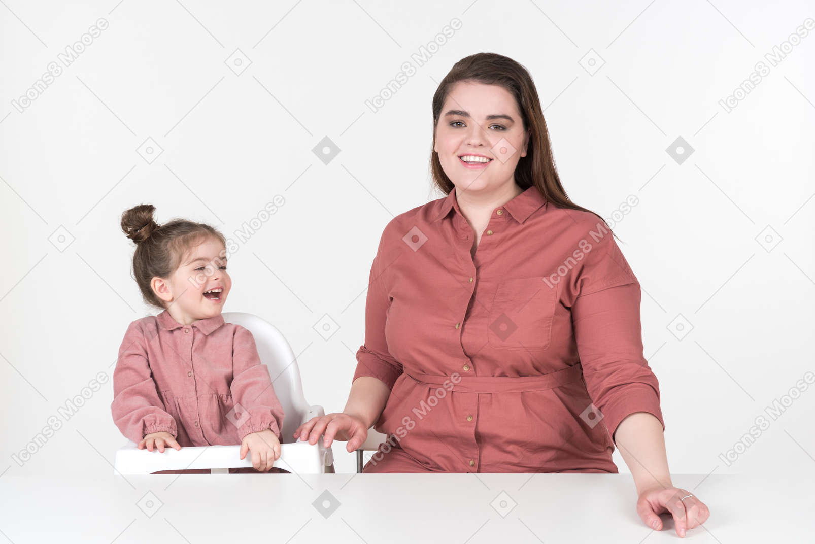 어머니와 그녀의 작은 딸, 빨간색과 분홍색 옷을 입고 저녁 식사 테이블에서 재미