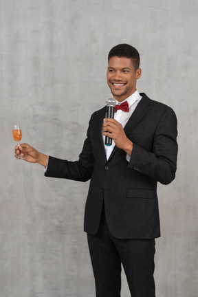 Homem com microfone sorrindo amplamente e levantando um copo