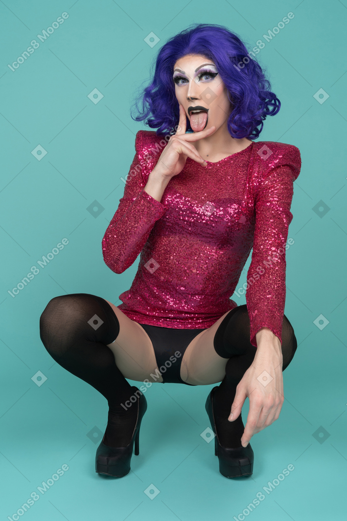 Portrait of a drag queen sticking out tongue & making a suggestive gesture while squatting
