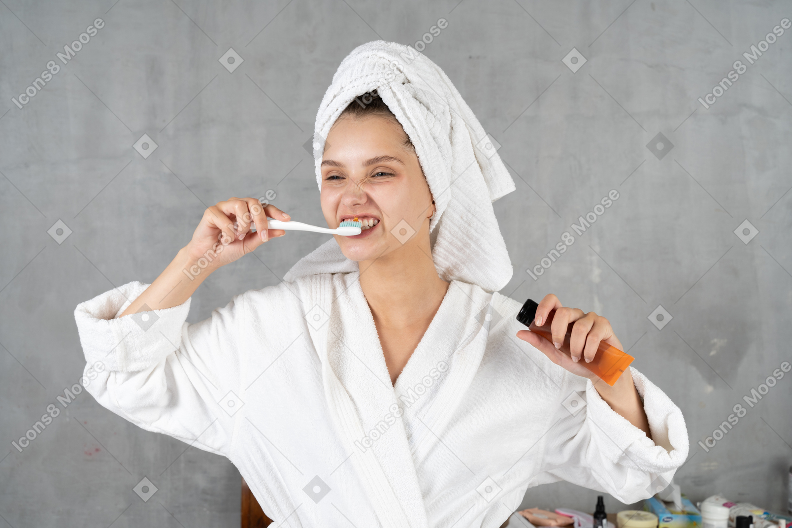 Woman in bathrobe making faces while brushing her teeth