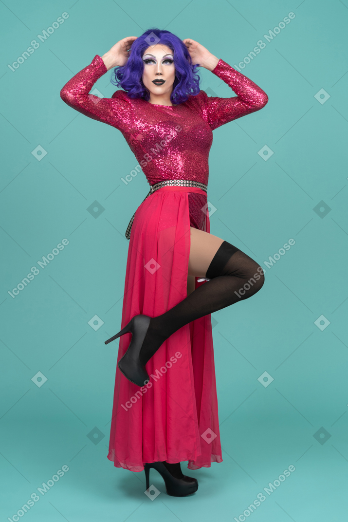Portrait of a drag queen in pink dress lifting a leg & touching head with both hands