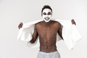 Un jeune homme noir avec une serviette de bain blanche autour de la taille et un autre sur les épaules qui vaquer à ses occupations