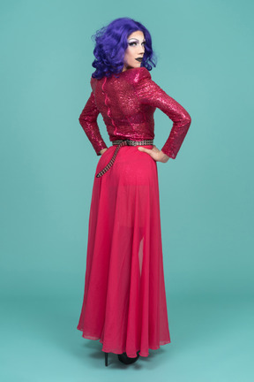 Vista posteriore di una drag queen in abito rosa in posa con le mani sui fianchi