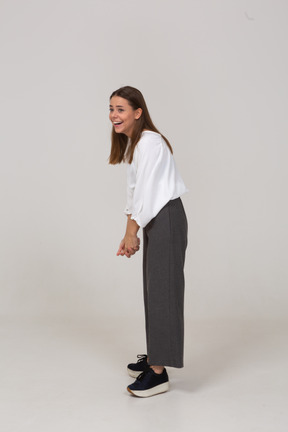 Vista laterale di una giovane donna ridente in abiti da ufficio protesa in avanti