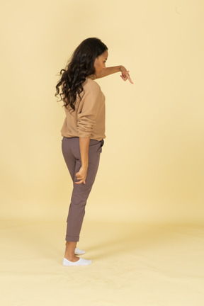 Vista posterior de tres cuartos de una mujer joven de piel oscura que señala con el dedo hacia abajo