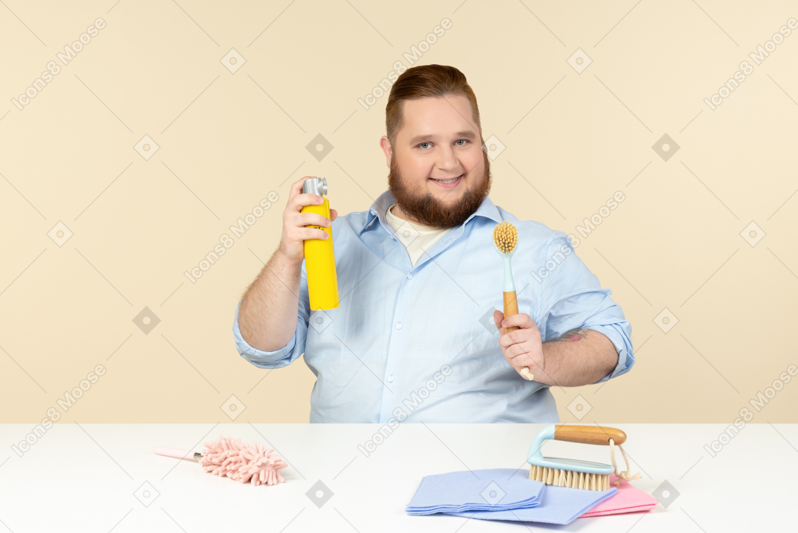 Joven amo de casa con sobrepeso sentado en la mesa y sosteniendo equipo de limpieza