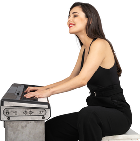 Vista lateral de uma jovem sorridente sentada de terno preto tocando piano