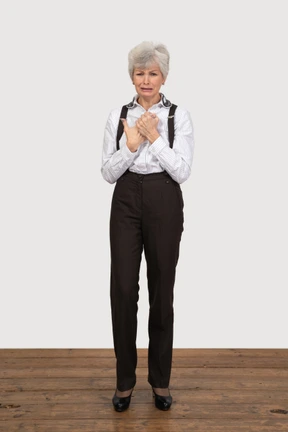 Front view of a crying old lady in office clothing holding hands together