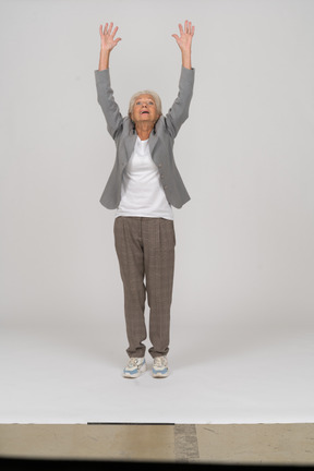 Front view of an old lady in suit standing on toes and raising arms