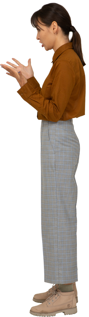Vista lateral de uma jovem mulher asiática questionadora de calça e blusa, levantando as mãos