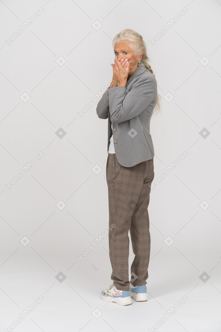 Rear view of a scared old lady in suit covering mouth with hands