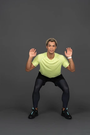Front view of a squatting dark-skinned young man raising hands