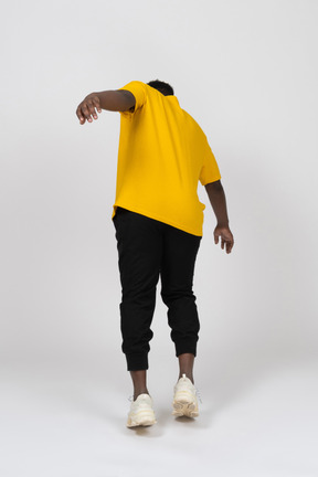 一个身穿黄色 t 恤的黑皮肤年轻男子的后视图，前倾并伸出手臂
