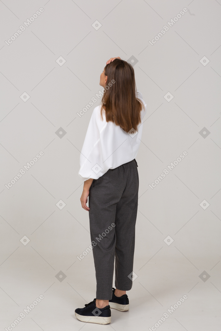 Three-quarter back view of a young lady in office clothing touching forehead