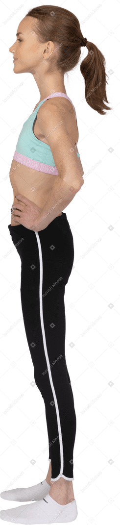 Seitenansicht eines jugendlich mädchens in der sportbekleidung, die hände auf hüften setzt und beiseite schaut