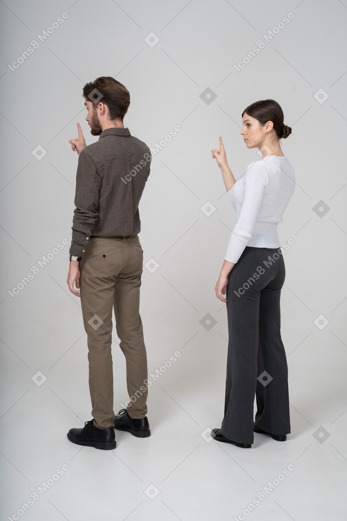 Three-quarter back view of a young couple in office clothing raising finger