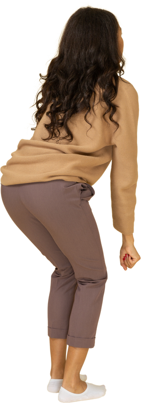 Vista posterior de tres cuartos de una mujer joven de piel oscura levantando pesas