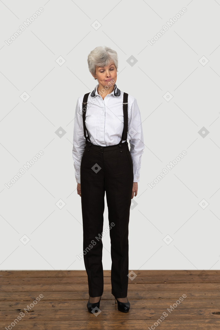 Front view of an old ashamed female in office clothes grimacing with her hands behind back