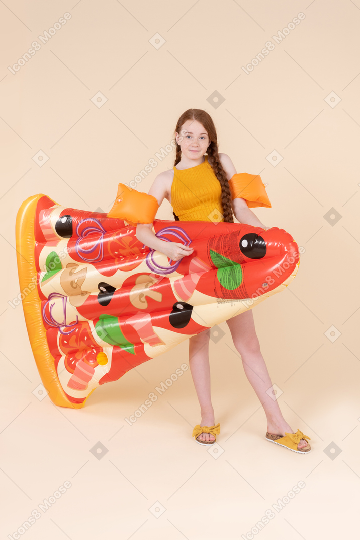 Teenage girl wearing arm floats and holding pizza mattress