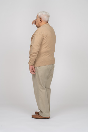 Vista lateral de un anciano con ropa informal tocando la nariz