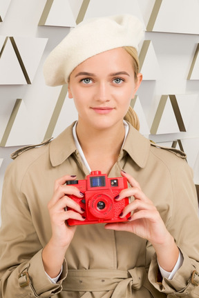 A woman in a trench coat holding a red camera