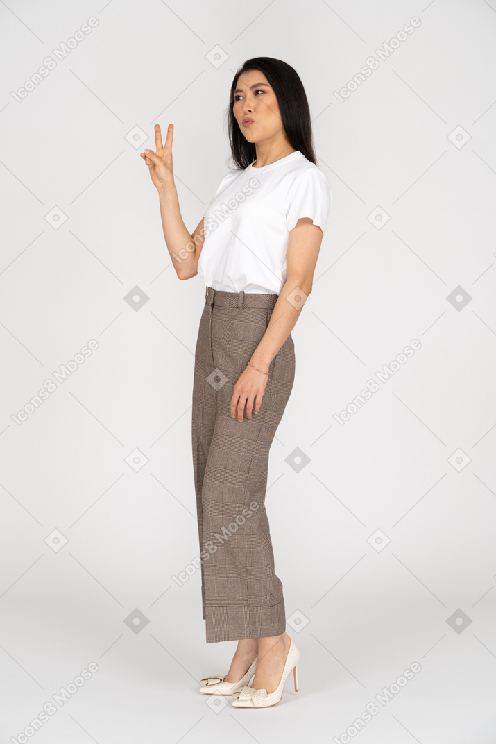 Vista di tre quarti di una giovane donna in calzoni che mostra il segno di pace